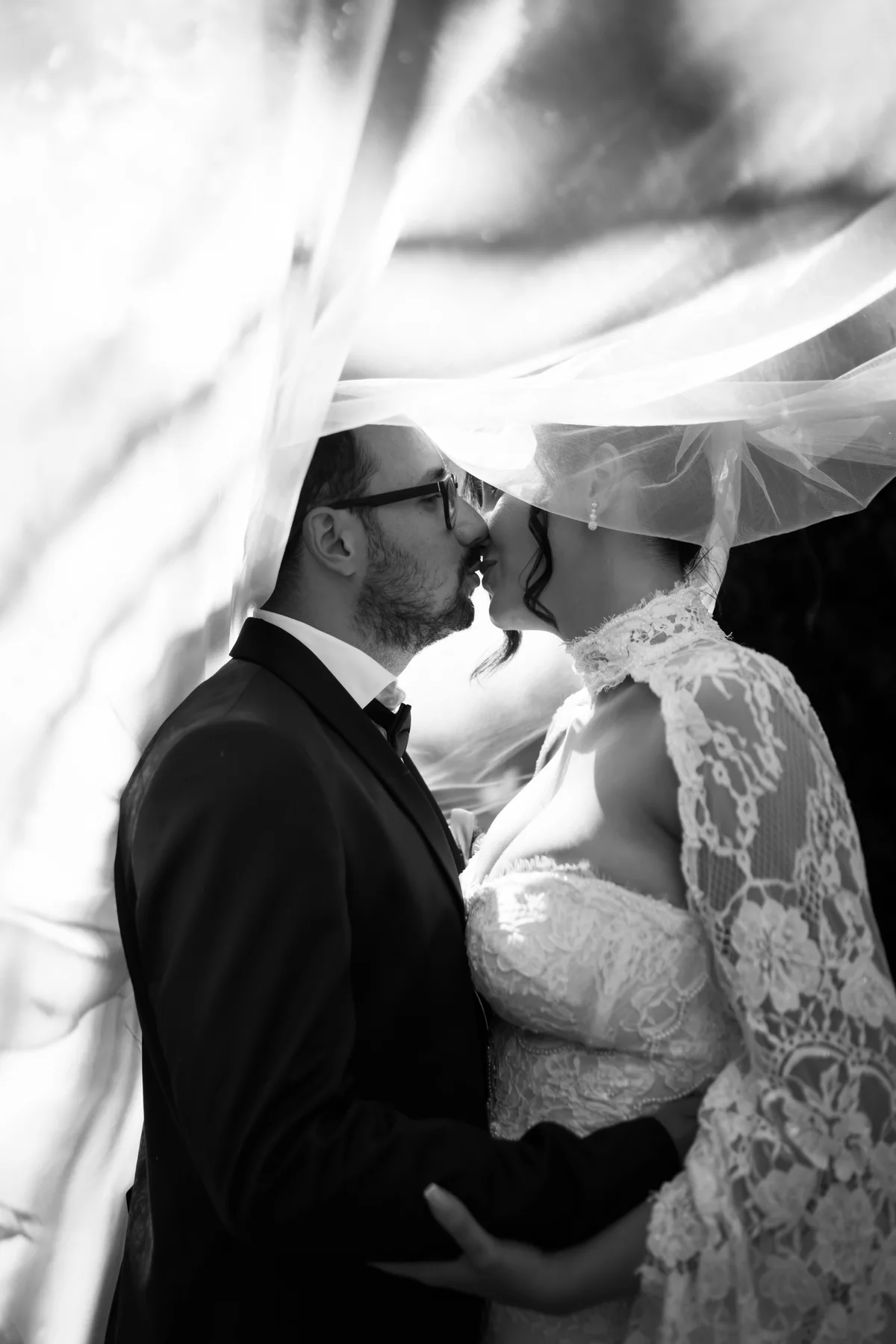 Crno-bela fotografija poljupca mladenaca ispod vela